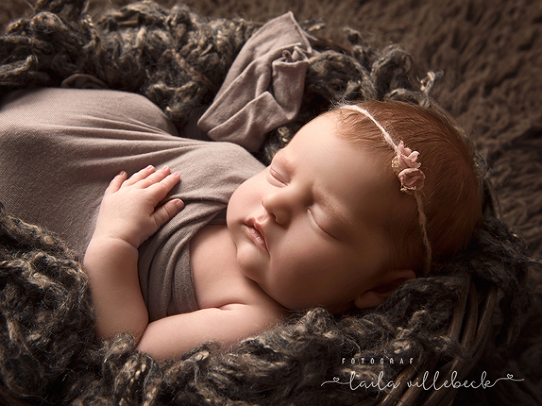 En nyfödd liten flicka ligger i en korg som står på en brun flokati.