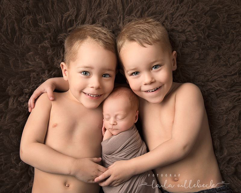 Två stolta tvillingbröder ligger och håller om nyfödd lillasyster