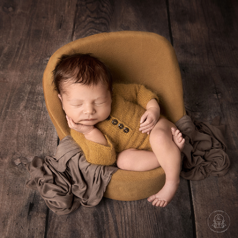 Viggo halvsitter sovandes i den specialanpassade fåtöljen som används specifikt för nyföddfotograferingar. Fåtöljens klädsel är utbytbar och här matchar klädseln den fina bodyn i semapsgult perfekt.