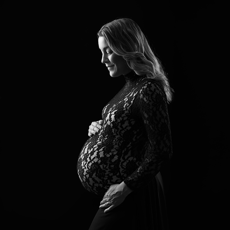 Vacker gravid kvinna i profil med vackert ljus och mot svart bakgrund. Bildern är svartvit.