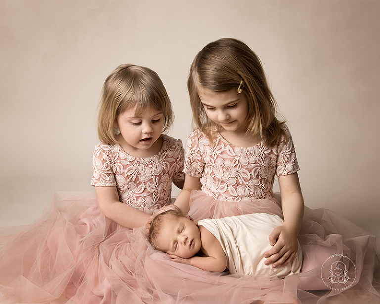 Syskonkärlek när två storasystrar tittar ner på sin nyfödda lillebror