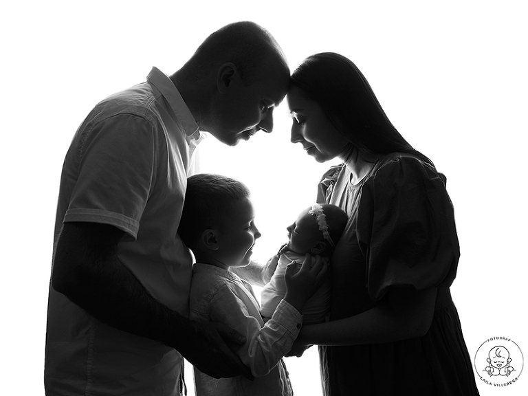 Familjebild i svartvitt under nyföddfotografering där hela familjen står i profil, mamma, pappa, storebror och lillasyster.