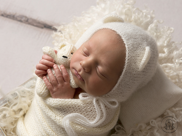Nyföddfotografering med liten tjej från Värnamo. Hon har en nallemössa på huvudet och håller i en liten miniatyrnalle i händerna