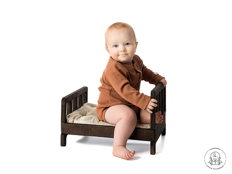 Bebis Algot sitter i en miniatyrsäng och ler ett sammanbitet leende in i kameran.