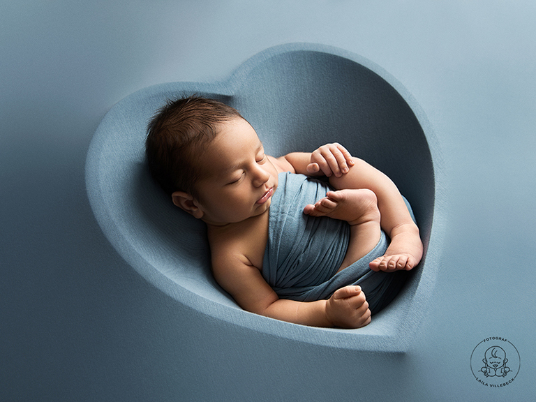 En otroligt vacker bild på en inlindad nyfödd på en blå filt med konturerna av ett hjärta.