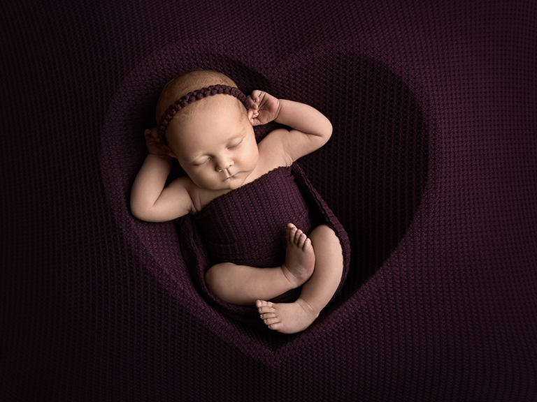 Nyföddfotografering i Norrköping med färgtema plum. Nyfödd poserad i ett hjärta