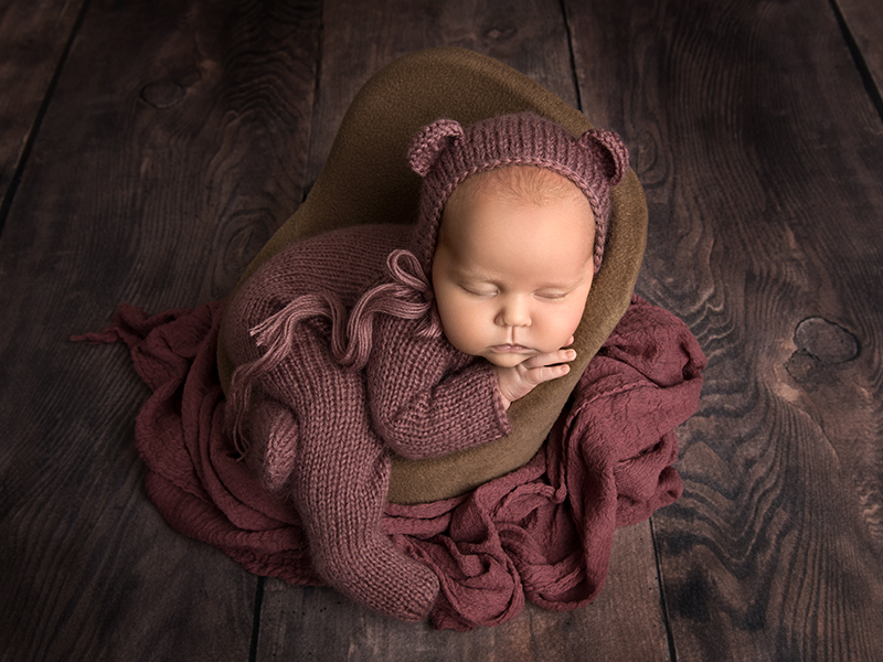 En 4-veckors bebis iklädd ett rosalila nalleset ligger på mage i en fåtölj och sover.