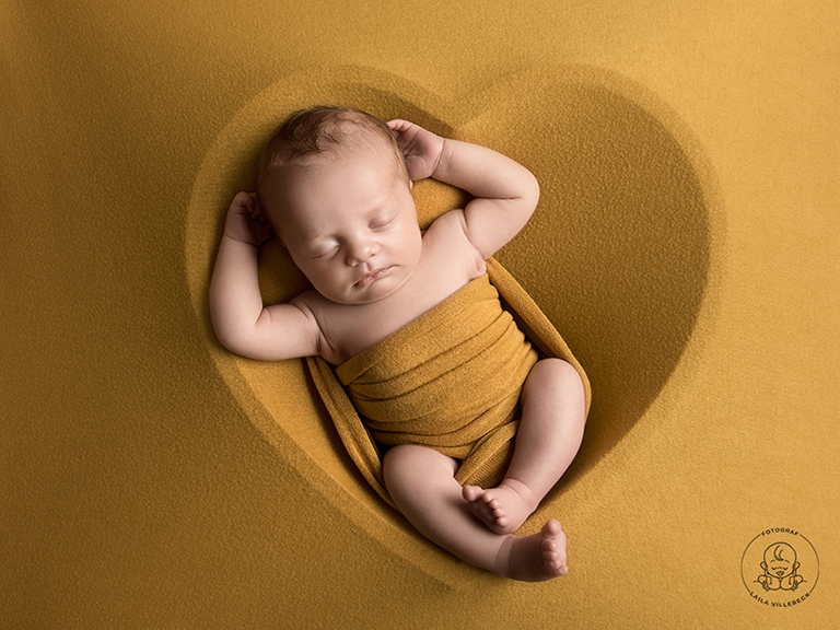 Att posera en nyfödd i ett hjärta blir väldigt fint. Här syns konturerna av ett hjärta genom en filt.
