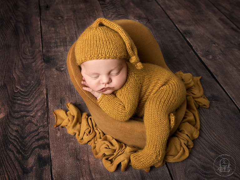 Nyföddfotograf i Linköping. Nyfödd poserad i magläge i miniatyrfåtölj. Färgerna går i höstiga senapsgult och brunt.