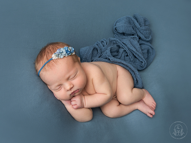 En traditionell nyföddposering, side pose, på beanbagen med blå filt och matchande wrap och hårband.