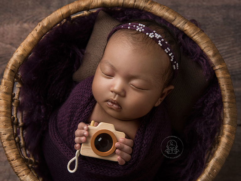 En nyfödd bebis som håller i en leksakskamera under sin nyföddfotografering