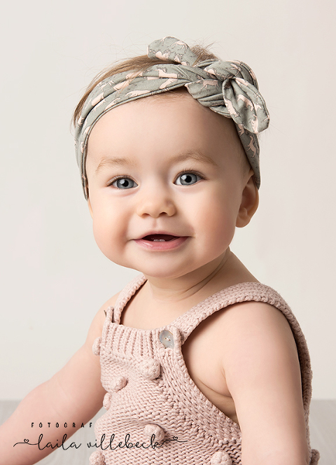Babyfotografering av glad liten tjej i rosa hemmastickad byxdress