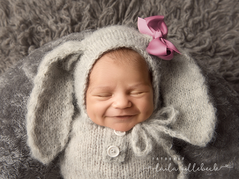 Nyfödd flicka med stort leende i grå kanindräkt