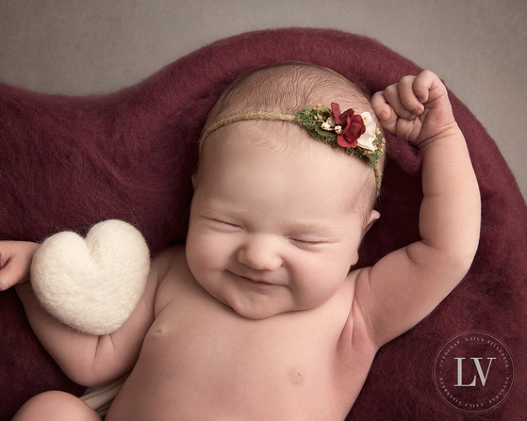 En leende nyfödd flicka med ett filtat hjärta i vitt
