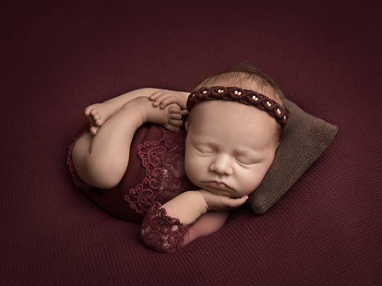 Nyfödd tjej sover i cool pose på en brun kudde och vinröd filt
