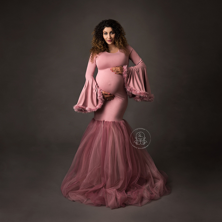 Ett helkroppsporträtt av en gravid vacker kvinna med en rosa klänning i sjöjungfrumodell med utsvängda ärmar.