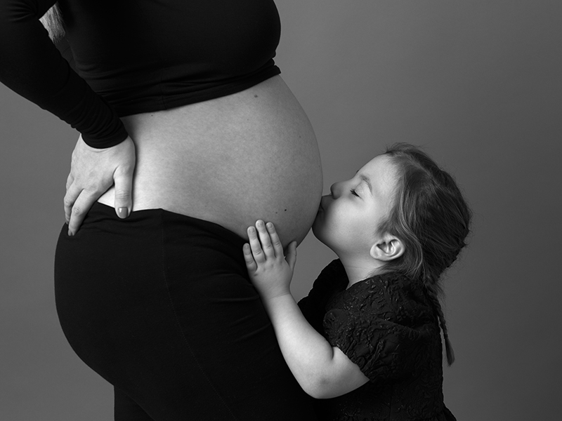 Gravidfotografering med storasyster som pussar magen där bebisen ligger och gror
